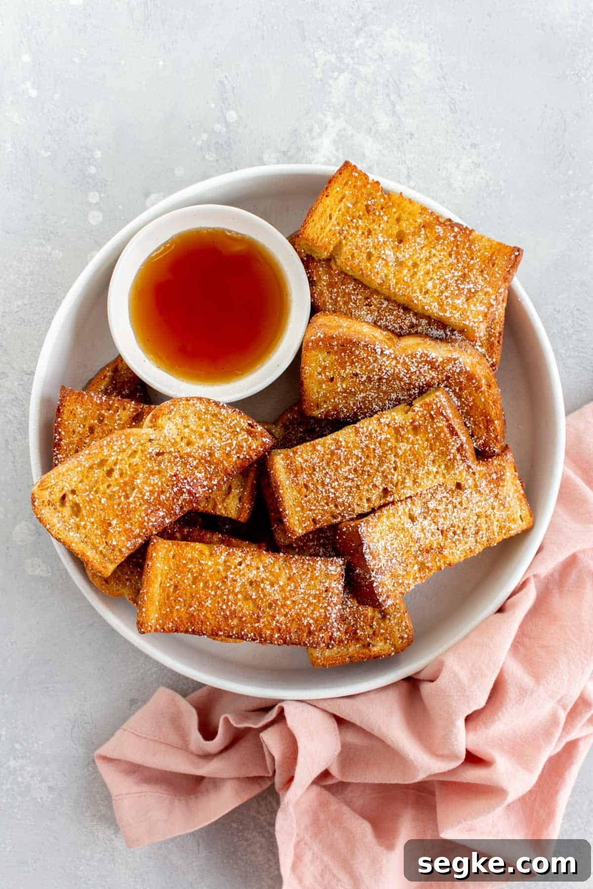 A plate of air fryer french toast sticks with powdered sugar dusted on top.