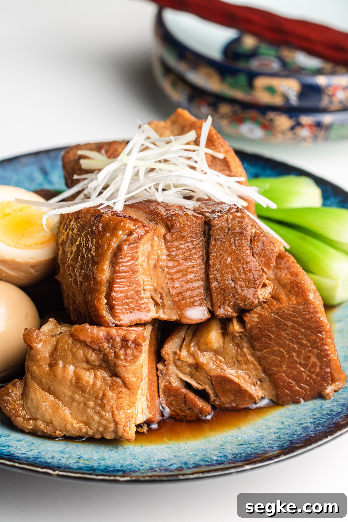 kakuni on a blue plate with scallion, eggs and bok choy