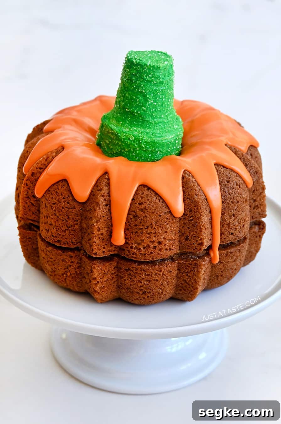 Spooky Halloween Dessert Recipes to Impress Guests 17 Easy Pumpkin Bundt Cake topped with a thick orange-colored glaze and a green sugar cone "stem" on a cake platter