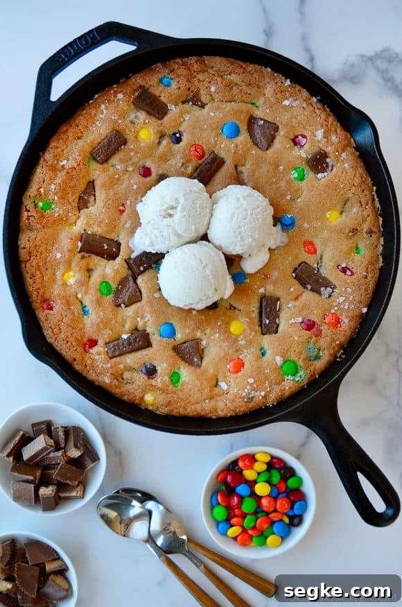 Spooky Halloween Dessert Recipes to Impress Guests 22 Leftover Halloween Candy Skillet Cookie topped with vanilla ice cream next to small bowls containing chocolate candy