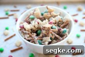 White Chocolate Peppermint Pretzel Cookie Bars Recipe 12 a white bowl full of pretzels and chex and m&ms covered in white chocolate. it also has peanuts in it. there is more of it scattered on the counter around the bowl