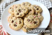White Chocolate Peppermint Pretzel Cookie Bars Recipe 8 The Best Peppermint Chocolate Chip Cookies stacked on a white plate with a white and blue squared striped pattern kitchen towel above it. In the bottom left corner is a partial picture of two candy canes.