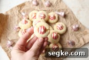 White Chocolate Peppermint Pretzel Cookie Bars Recipe 9 A hand holding a peppermint kiss cookie above more peppermint cookies and Peppermint Hershey Kisses all sitting on a crumpled brown paper.