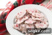 White Chocolate Peppermint Pretzel Cookie Bars Recipe 10 Candy cane white chocolate pretzel crisps in a bowl with a green and red patterned napkin and candy canes surrounding the bowl from the bottom left up to the top right corner.