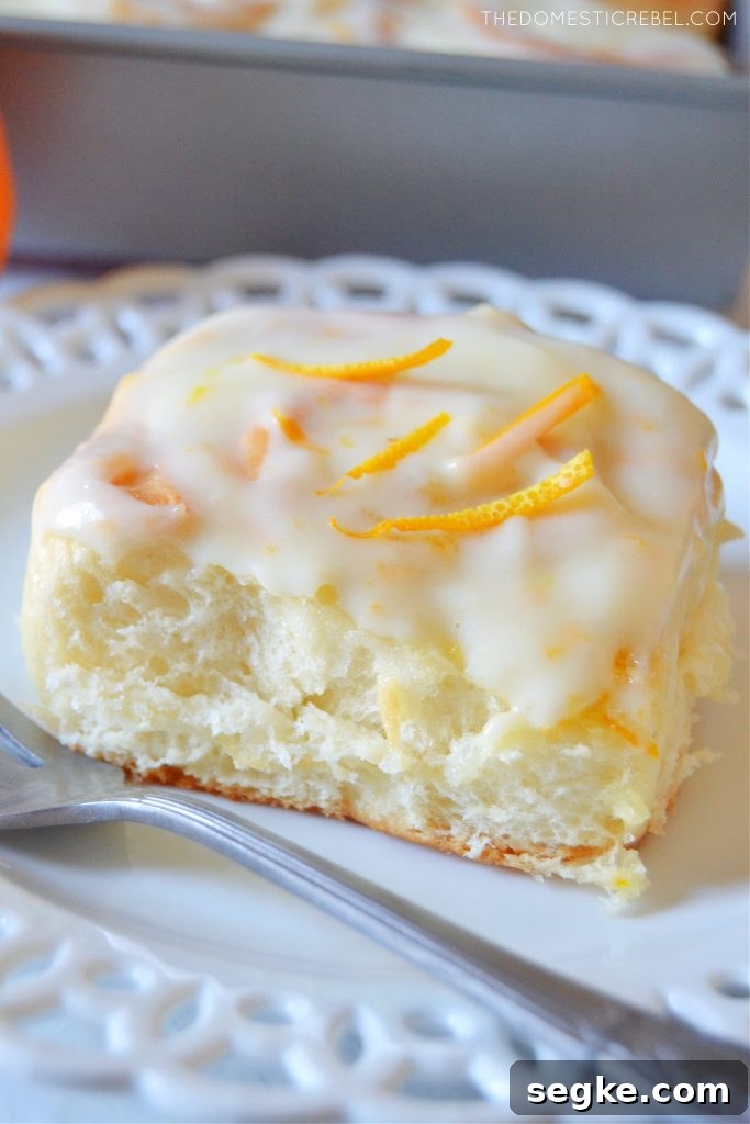 Zesty Orange Glazed Sweet Rolls Recipe 2 An orange sweet roll on a white lace plate with a silver fork