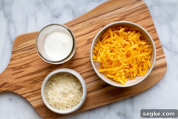 a bowl of shredded cheddar cheese, shredded parmesan cheese and heavy cream on a wooden board