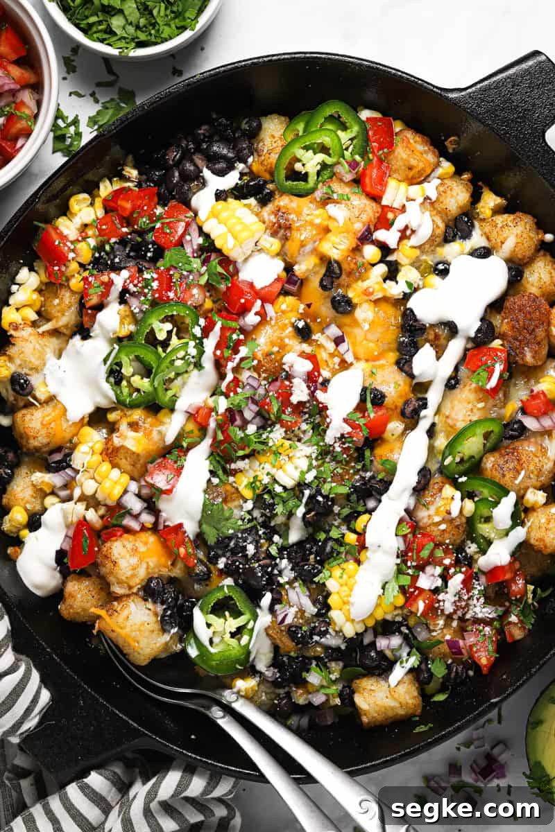 Large cast iron skillet with loaded vegetarian totchos garnished with cilantro and sour cream 