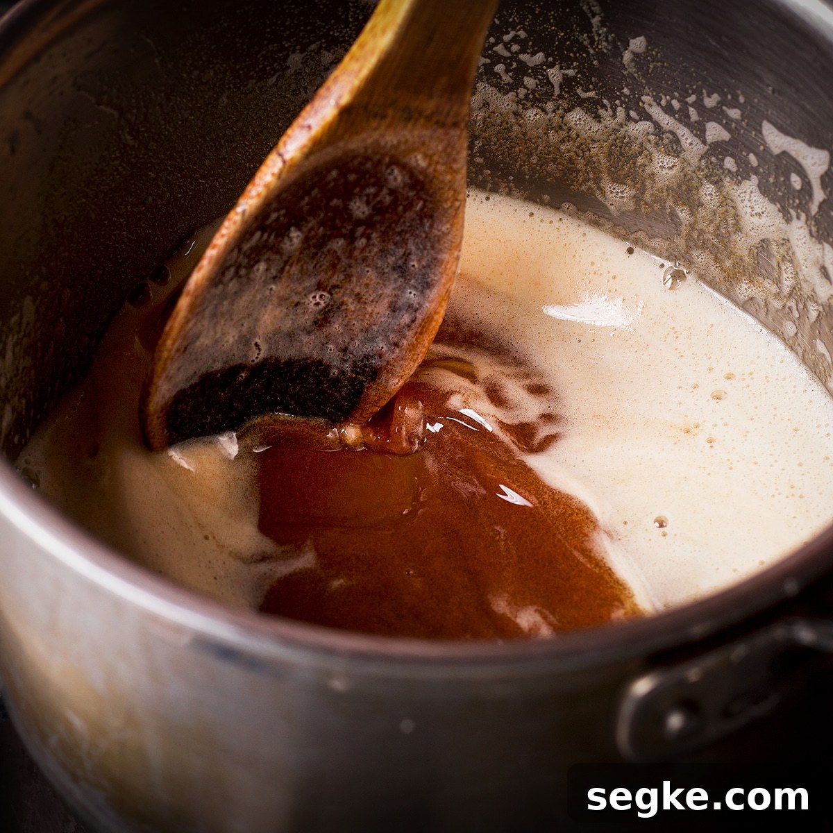 Someone using a wood spoon to stir browned butter in a saucepan.