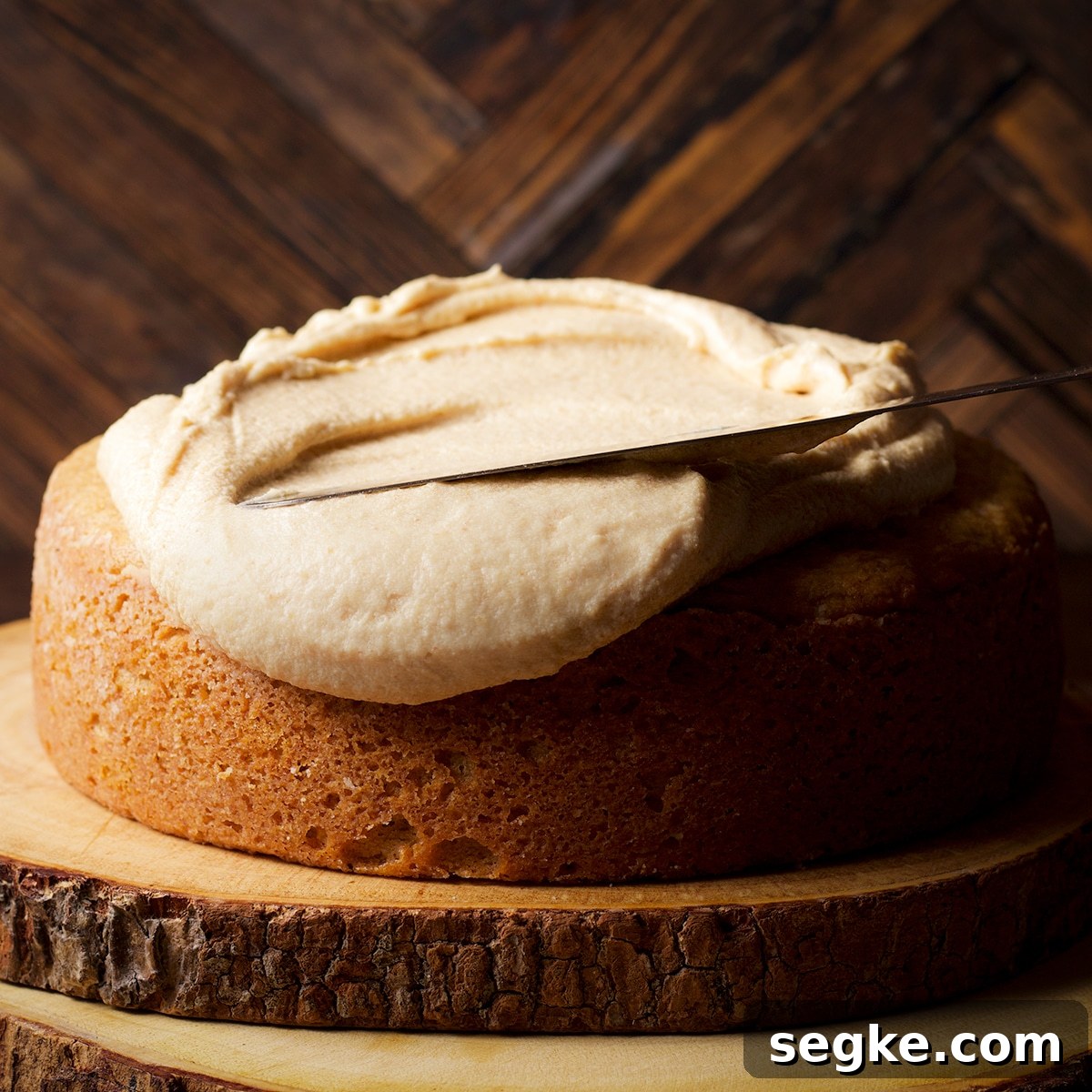 Using a flat icing spatula to spread maple miso brown butter frosting over a round one layer cake.