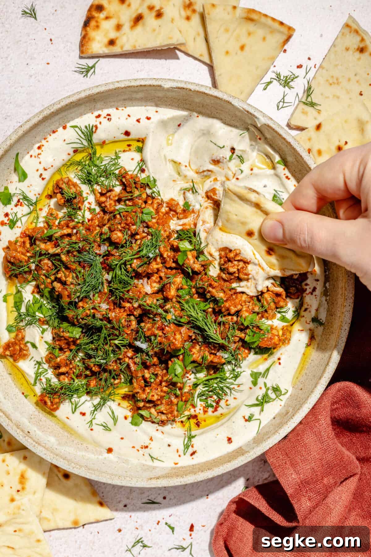 Labneh with Spicy Lamb and Roasted Eggplant Recipe 6 Spicy Lamb and Eggplant Labneh in a low bowl. Hand dipping pita into bowl.