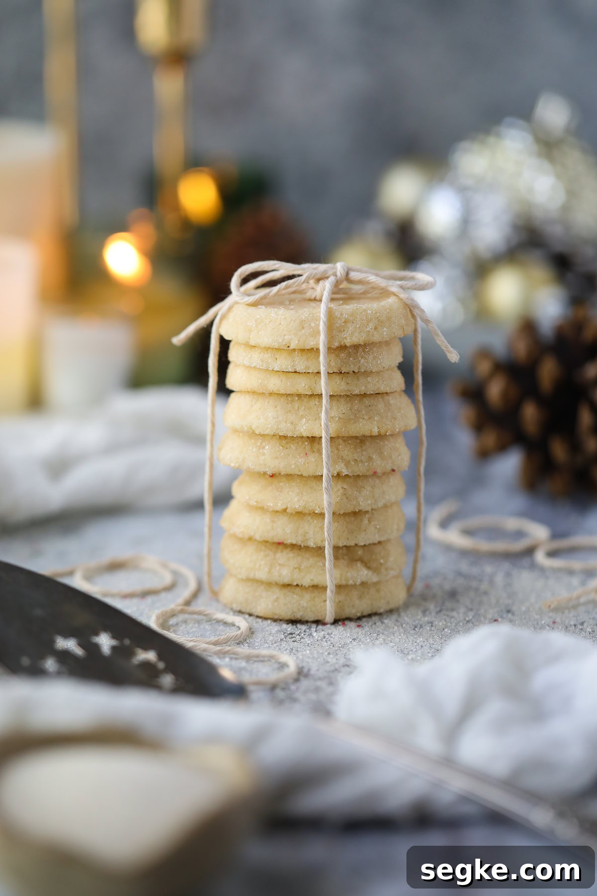 Cardamom butter cookies stacked on a table with pinecones and candles in the background.