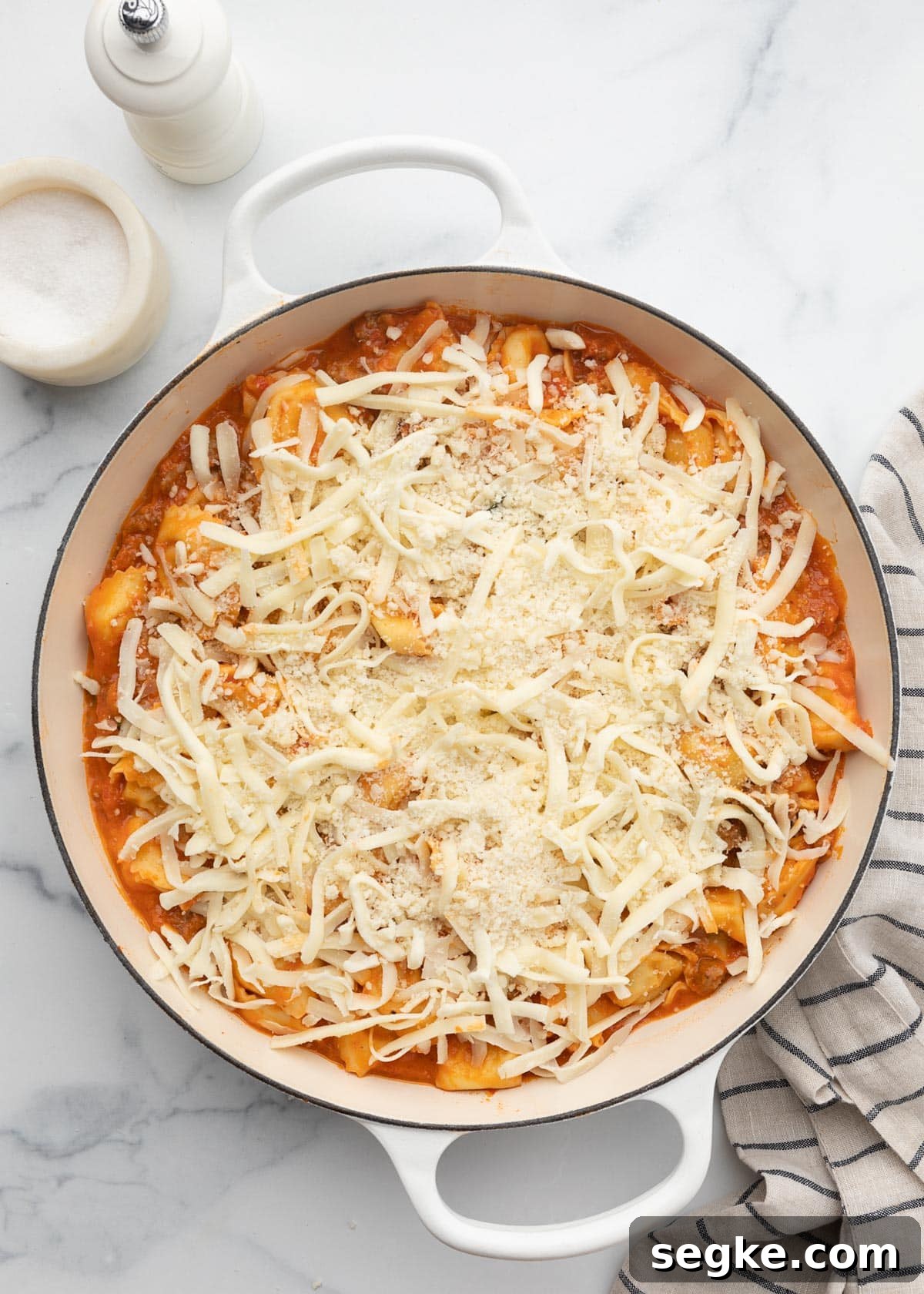 unbaked cheese topped tortellini casserole in a white enameled cast iron pan
