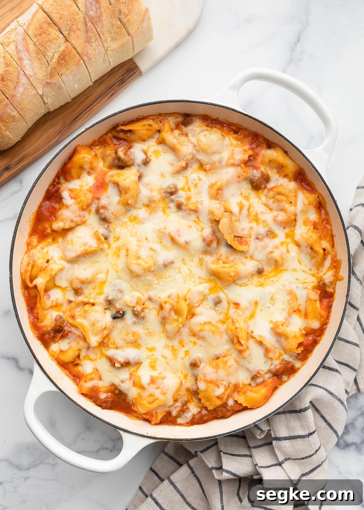 overhead of a tortellini sausage bake with melted mozzarella on top in a white enameled cast iron pot on a marble board