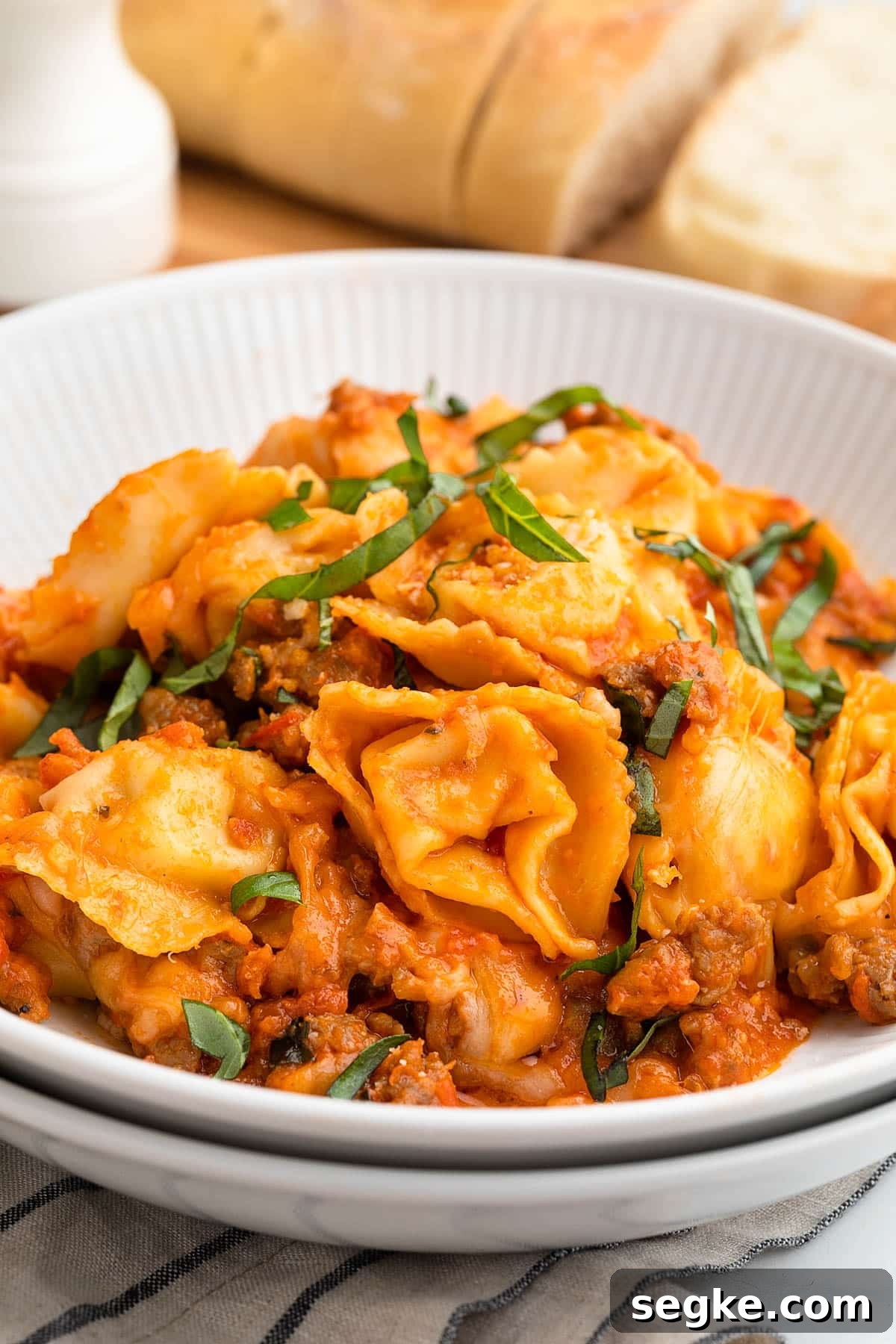 baked tortellini with sausage served in a double-stacked white pasta bowl with a garnish of julienned basil