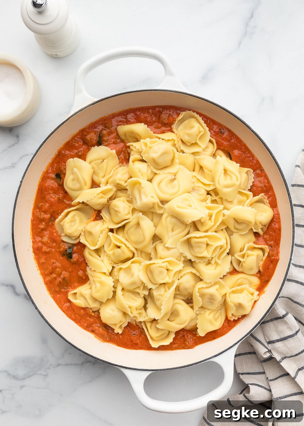 cooked tortelloni on top of marinara sauce in a white enameled cast iron pan