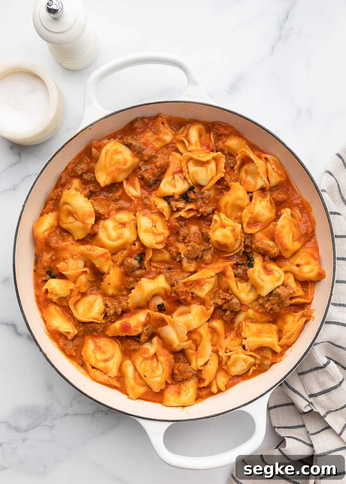 cooked tortellini stirred into sausage tomato sauce in a white enameled cast iron pan