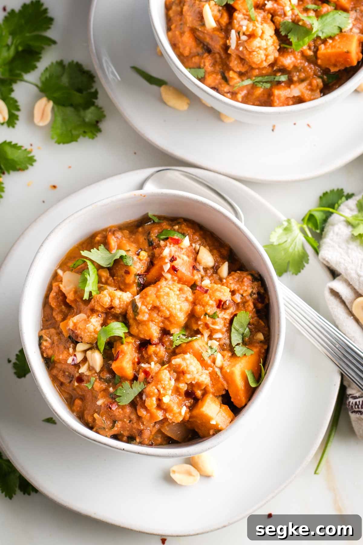 Bowl of chunky tomato based stew with fresh herbs and peanuts.
