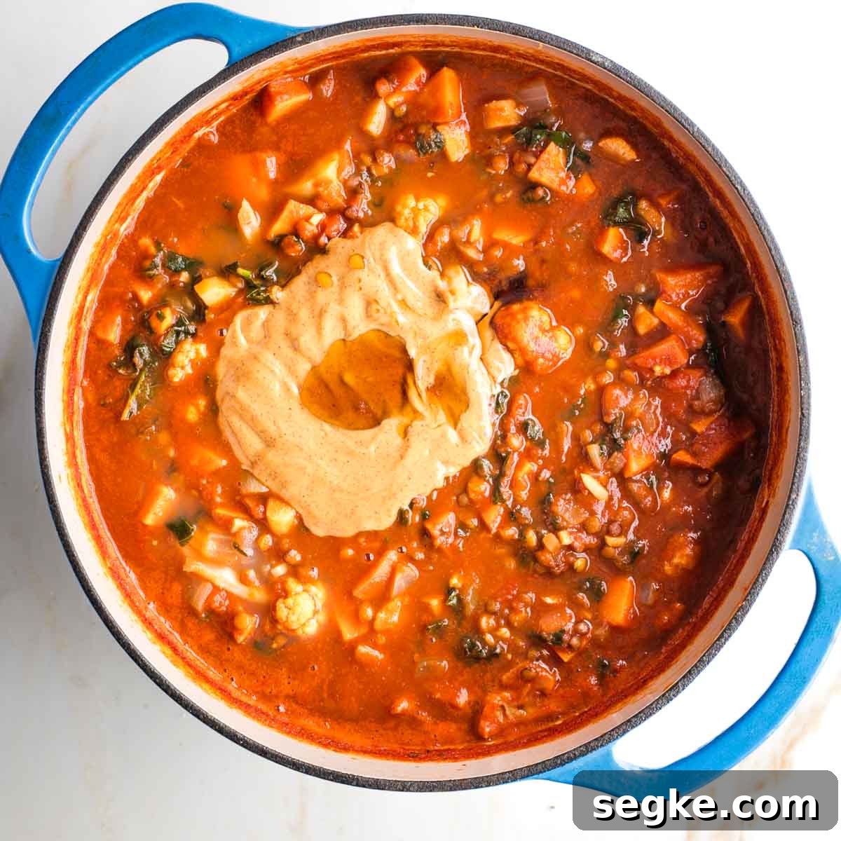 Peanut butter and maple syrup on top of a pot of tomato based veggie stew.