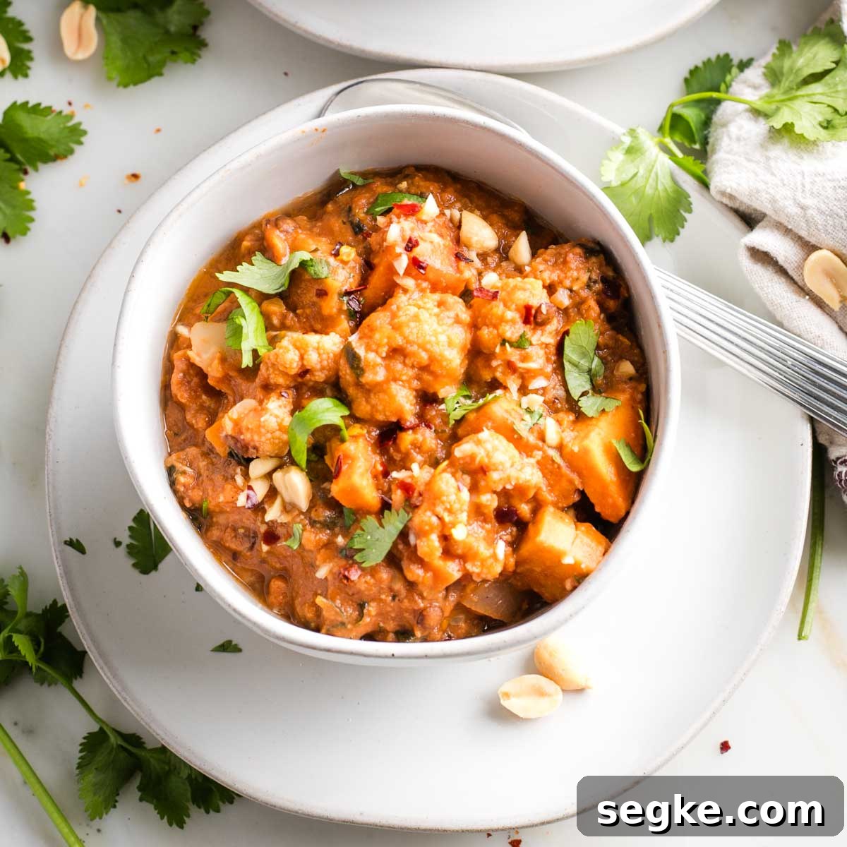 Bowl of chunky vegetable stew, garnished with fresh herbs and crushed peanuts.