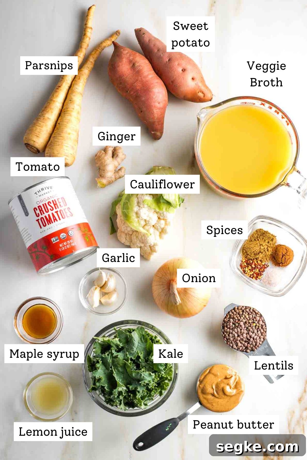 Labeled ingredients like sweet potatoes, veggie broth, canned tomatoes, garlic, ginger, kale, peanut butter and lentils to make a vegan stew.