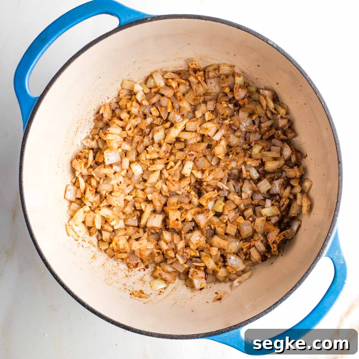 Spices coating onions, ginger and garlic inside a dutch oven.