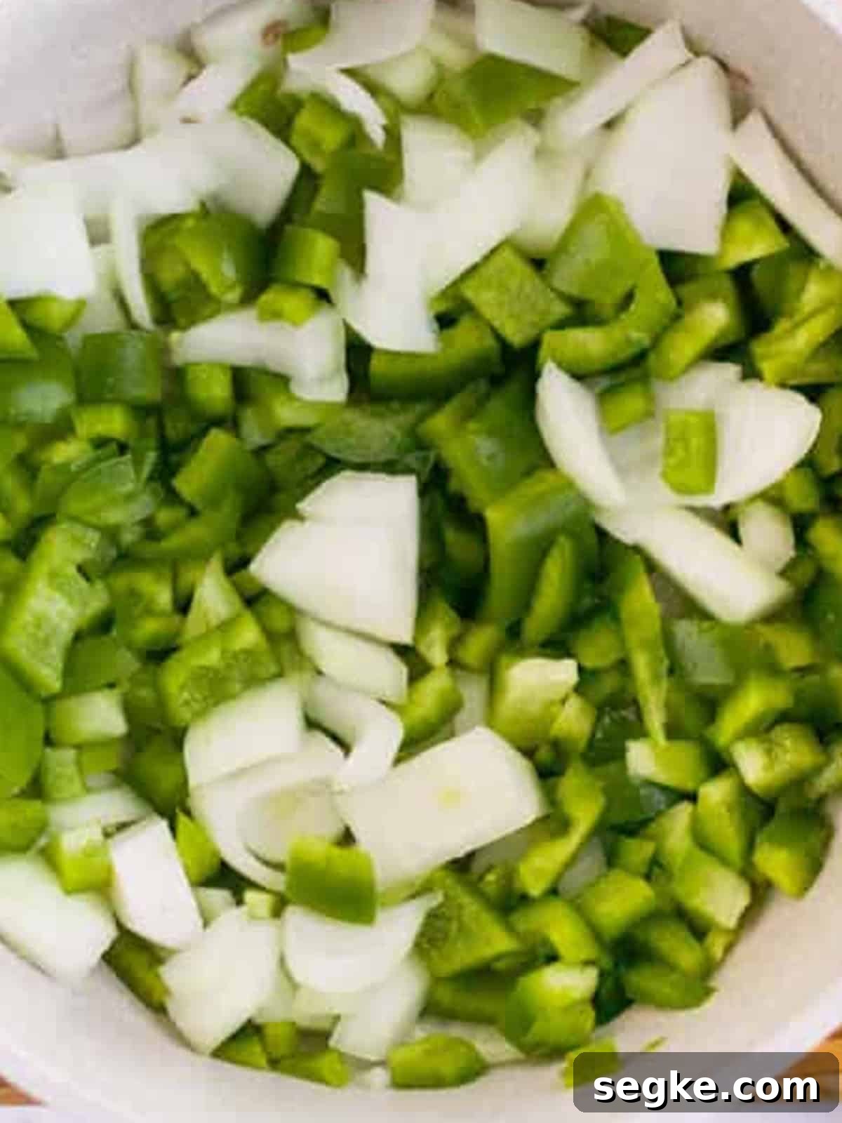 Chopped green bell peppers and onion cooking in a pot for stuffed pepper soup.