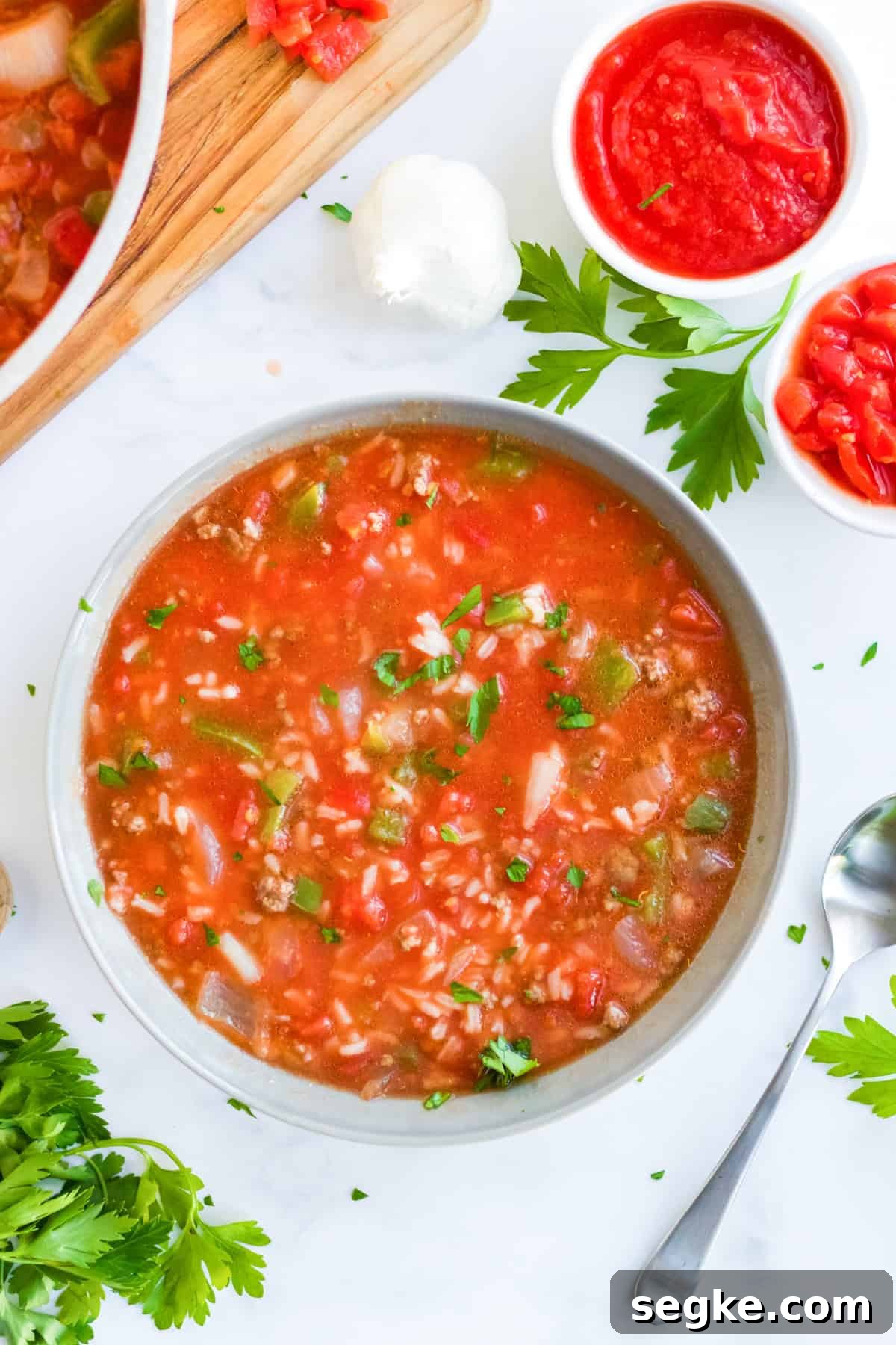 A white bowl of hearty stuffed pepper soup with a spoon, topped with fresh parsley.