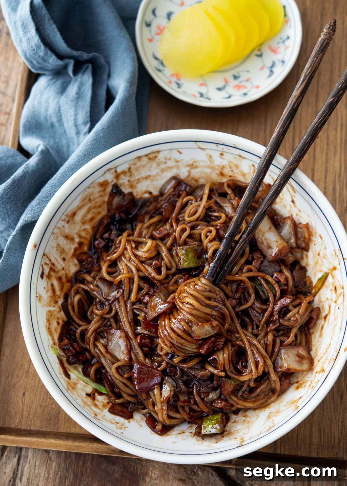 Jajangmyeon Recipe: Korean Black Bean Noodles 3 A pair of chopsticks twirling black bean noodles in a bowl.