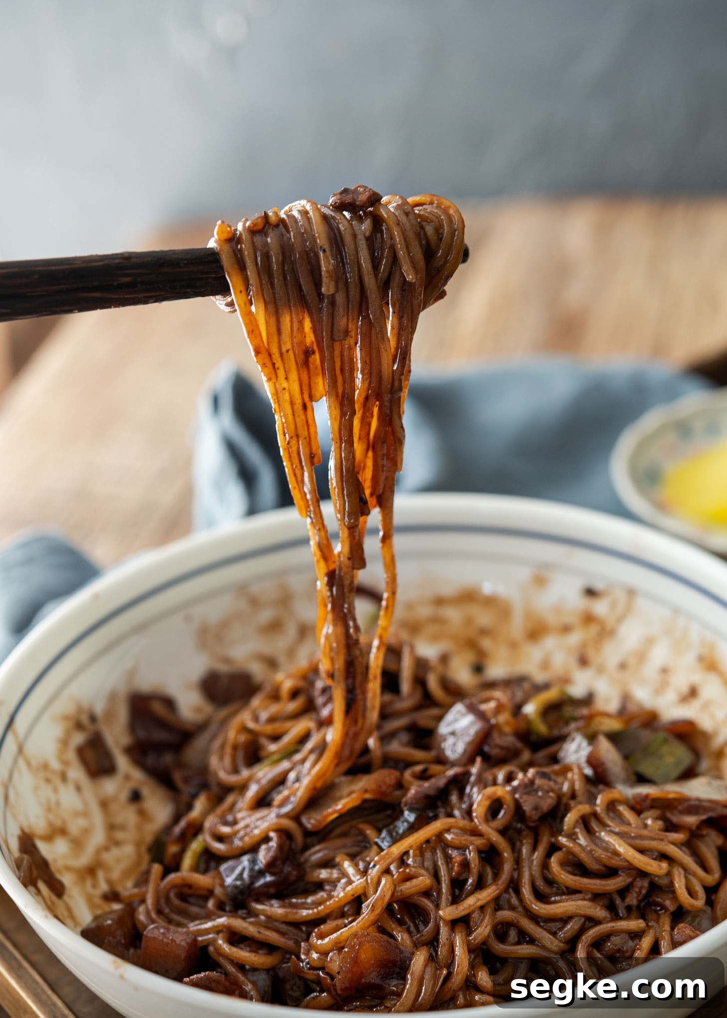 Jajangmyeon Recipe: Korean Black Bean Noodles 7 A pair of chopsticks holding up black bean noodles.