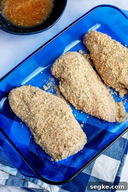 Breaded chicken breast in a blue glass baking dish before going in the oven.