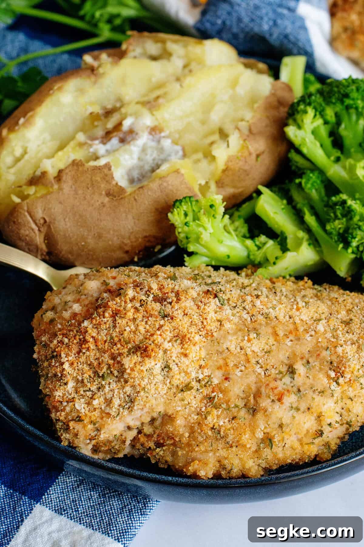 Golden brown oven-fried chicken breast on a plate with a baked potato and broccoli.