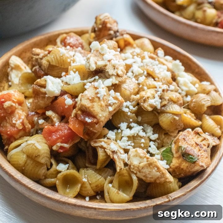 Bowl of shell pasta with tomatoes, feta cheese, and balsamic vinegar with text Mediterranean Chicken with Pasta