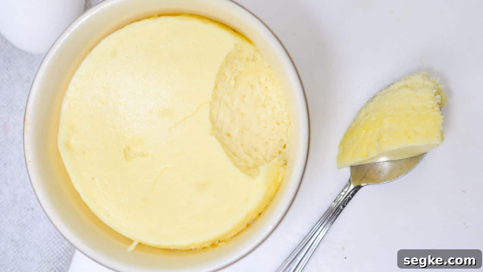 A ramekin of creamy, smooth cheesecake with a spoon resting beside it, taking out a scoop on a white background.