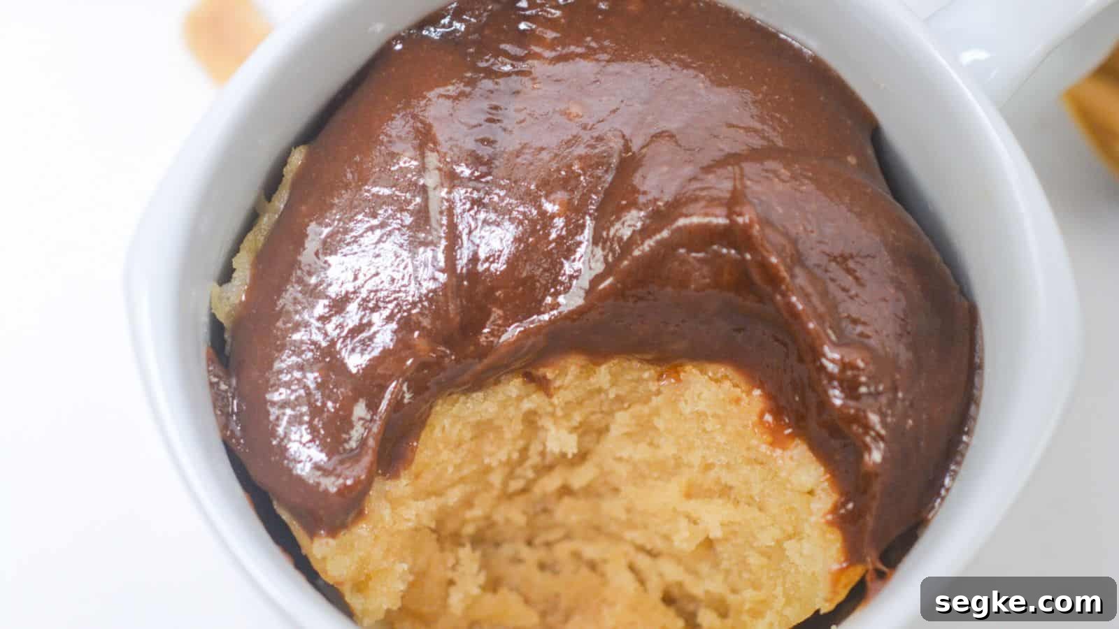 A peanut butter mug cake topped with a smooth, glossy chocolate sauce, viewed from above.