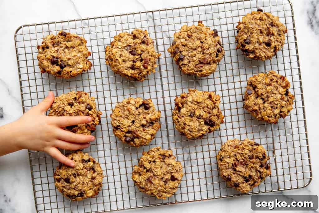 Banana Oat Breakfast Cookies - Gluten-Free Vegan 2 A kid's hand grabbing a banana oatcake cookie off of a cooling rack.