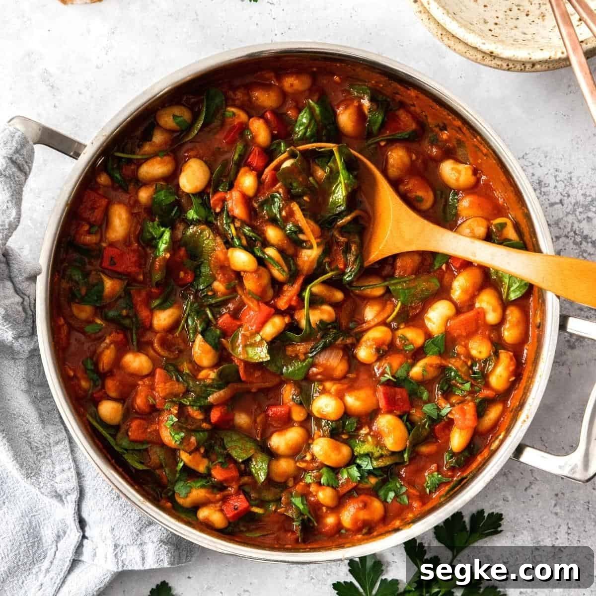 Round saucepan of butter bean stew, with a wooden spoon sitting in the pot.