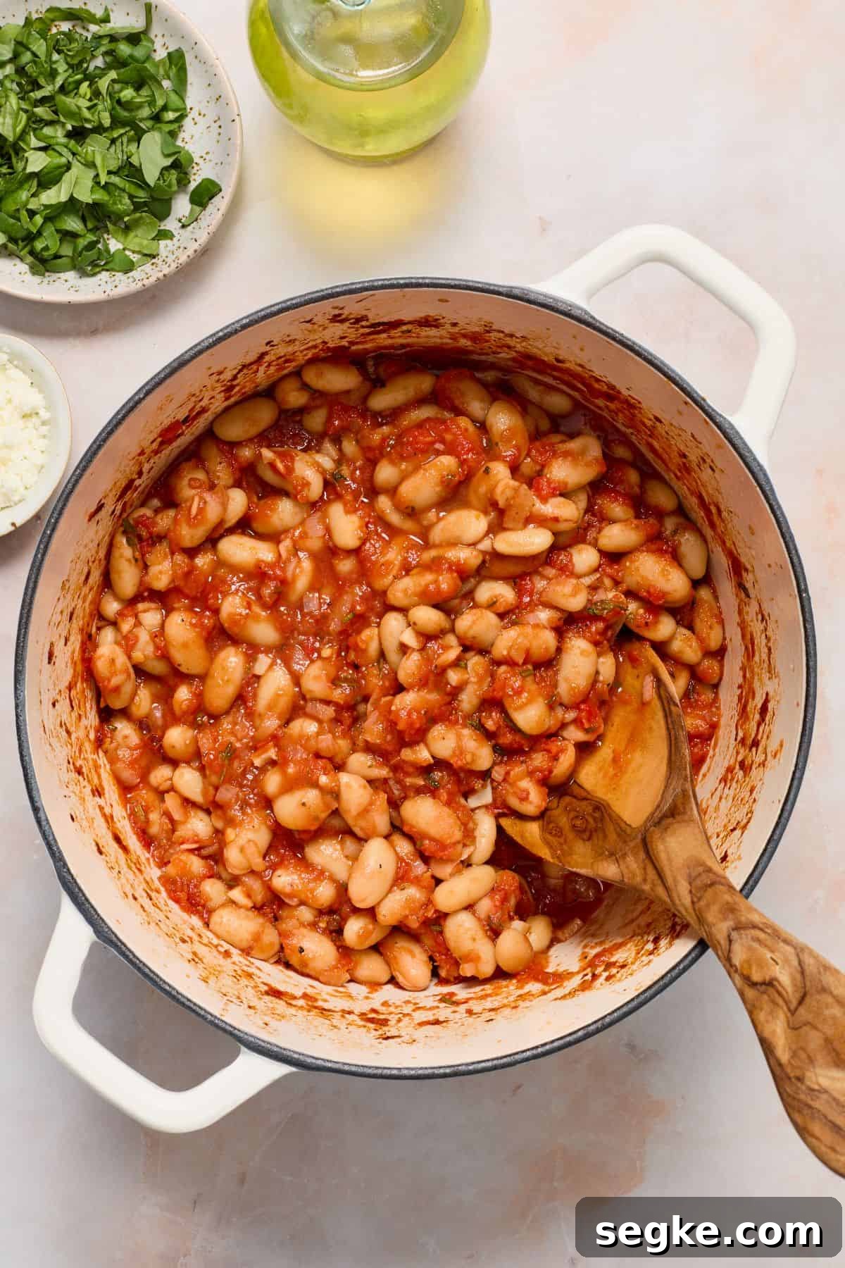 Saucepan with Mediterranean Baked Beans, with a wooden spoon resting in the pot.