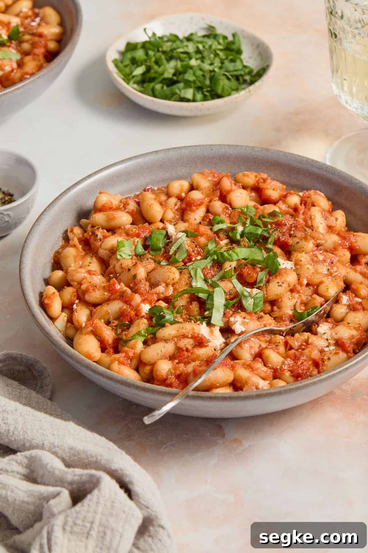 Round grey bowl with a serve of Mediterranean Baked Beans, garnished with torn fresh basil.