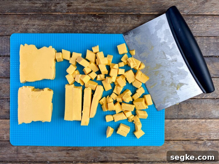 A board scraper showing how to cut up chunks of Velveeta cheese into cubes on a cutting board.