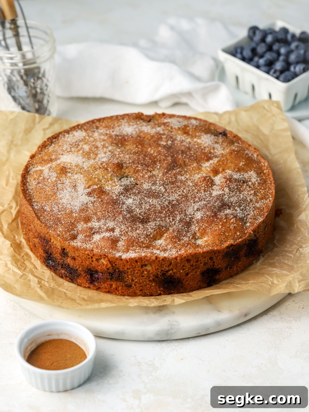 Moist Blueberry Cornmeal Cake Recipe 5 Blueberry cornmeal cake with cinnamon sugar on top next to a bowl of blueberries.