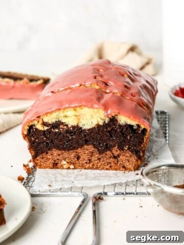 Moist Blueberry Cornmeal Cake Recipe 7 A loaf cake with chocolate, vanilla, and strawberry layers and strawberry icing on a rack.