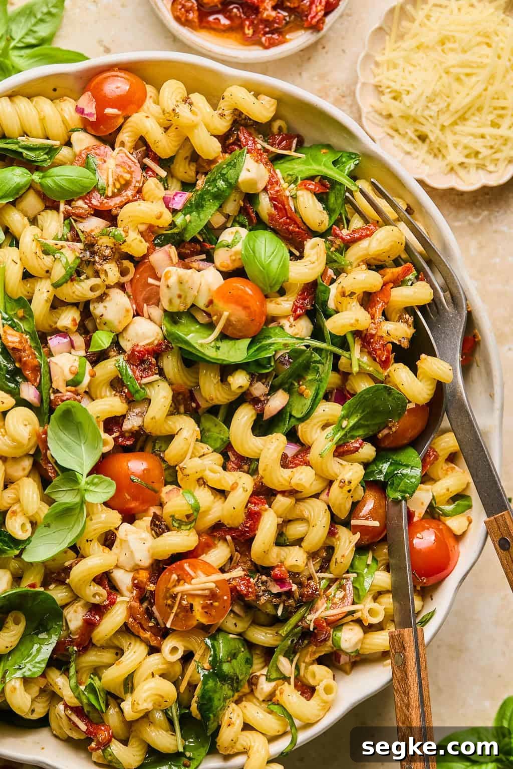 Sun dried tomato pasta salad topped with chopped basil and spoon and fork propped in the bowl.