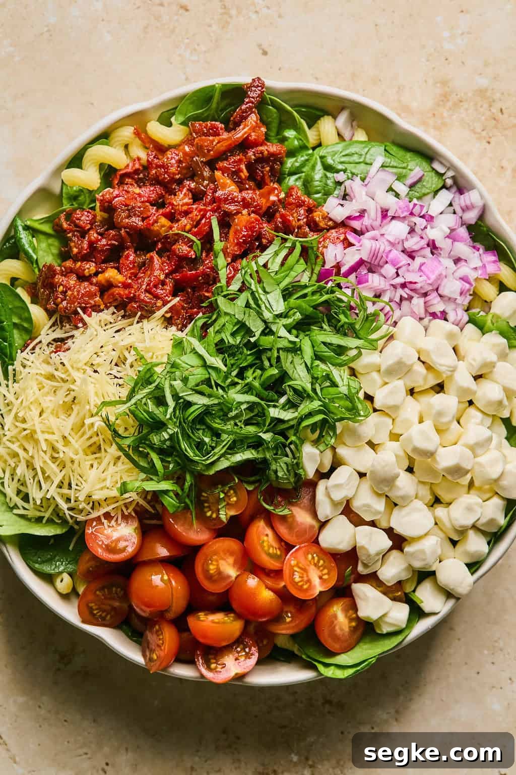 Pasta in bowl topped with mozzarella pearls, onions, shredded parmesan and other ingredients.