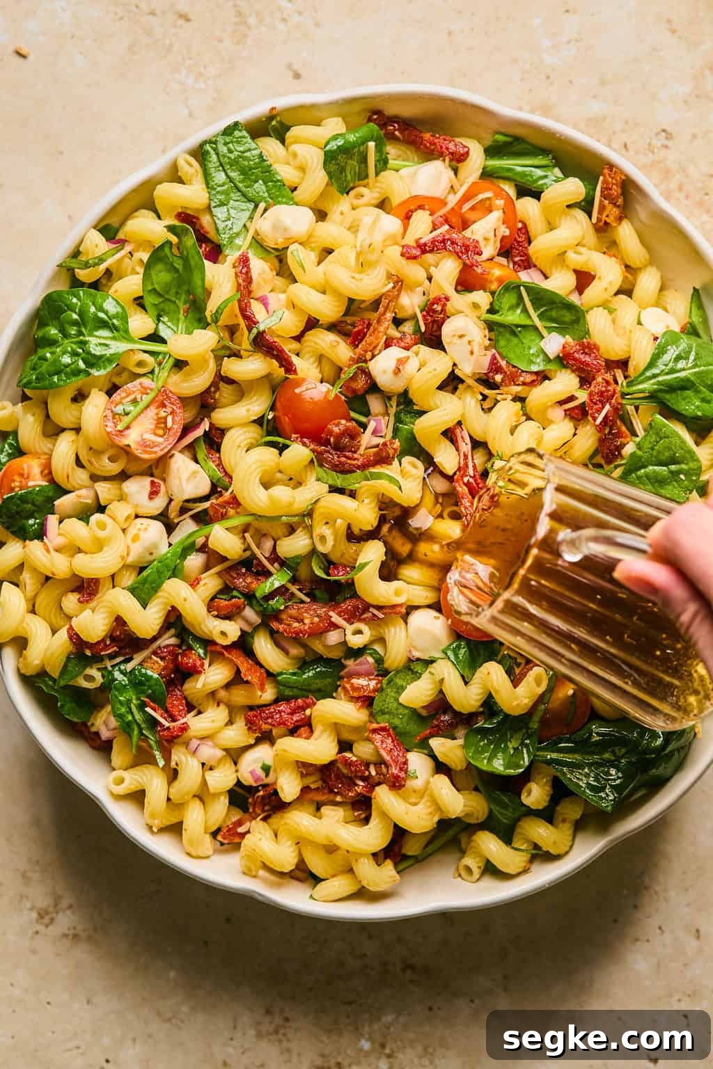 Pasta salad with dressing being poured over top.