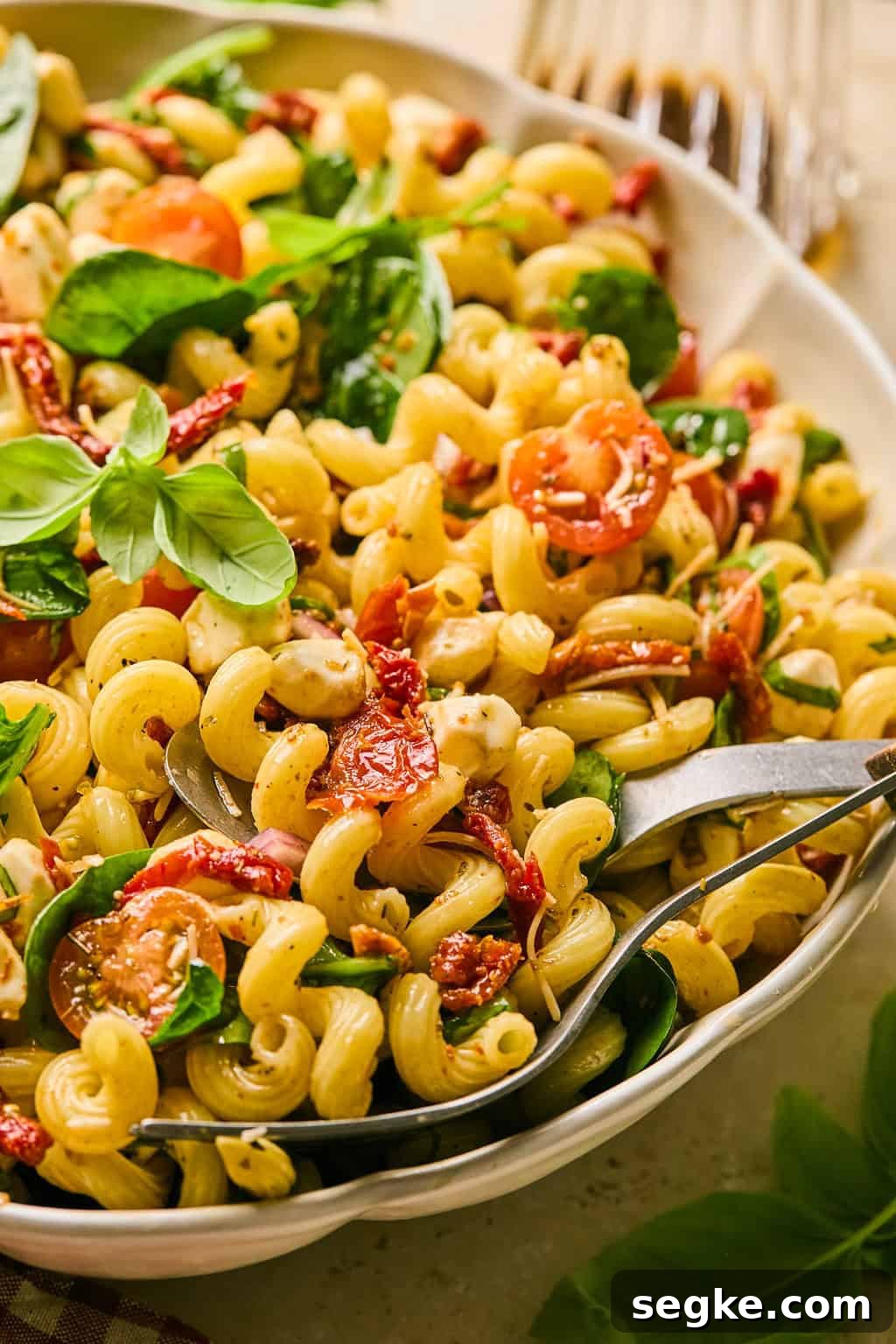 Sun-dried tomato pasta salad in white dish topped with freshly chopped basil.