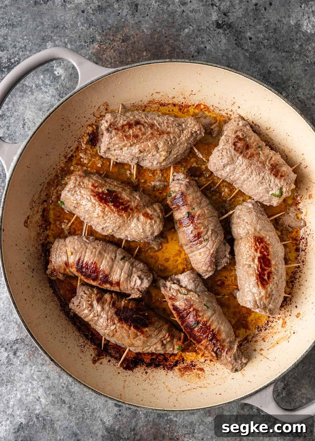 closeup overhead: rolled beef braciole with toothpicks searing in olive oil in skillet