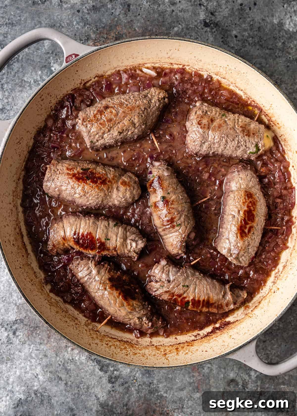 closeup overhead: red wine added to the rolled beef braciole in skillet