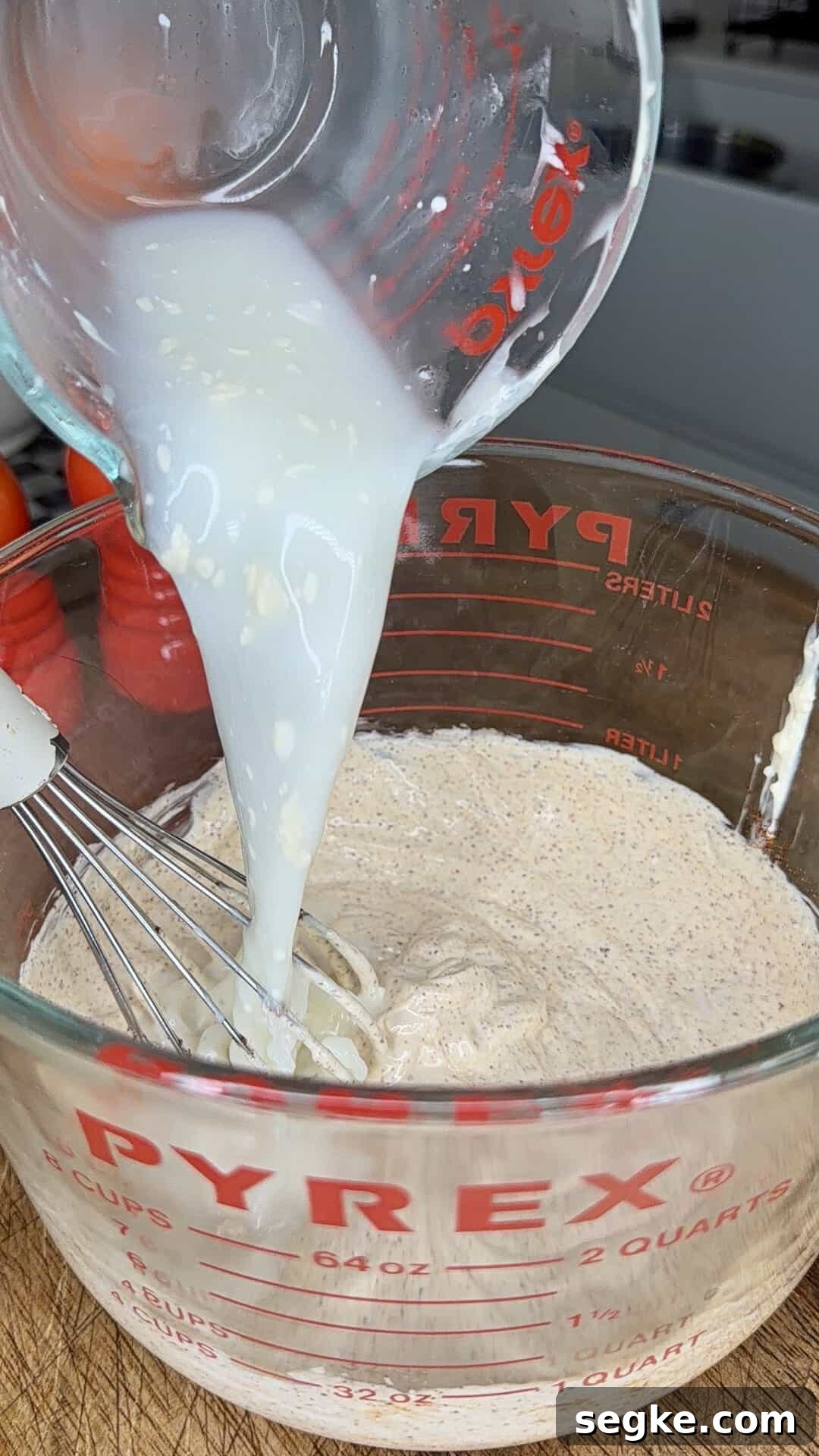 Mexican Street Corn Pasta Salad Recipe with Cotija and Lime 7 A glass measuring cup pours a white liquid into another glass measuring cup containing a beige, speckled mixture being whisked. Both cups are labeled Pyrex.