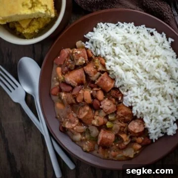 Red beans and sausage next to rice on brown plate with cornbread on the side.