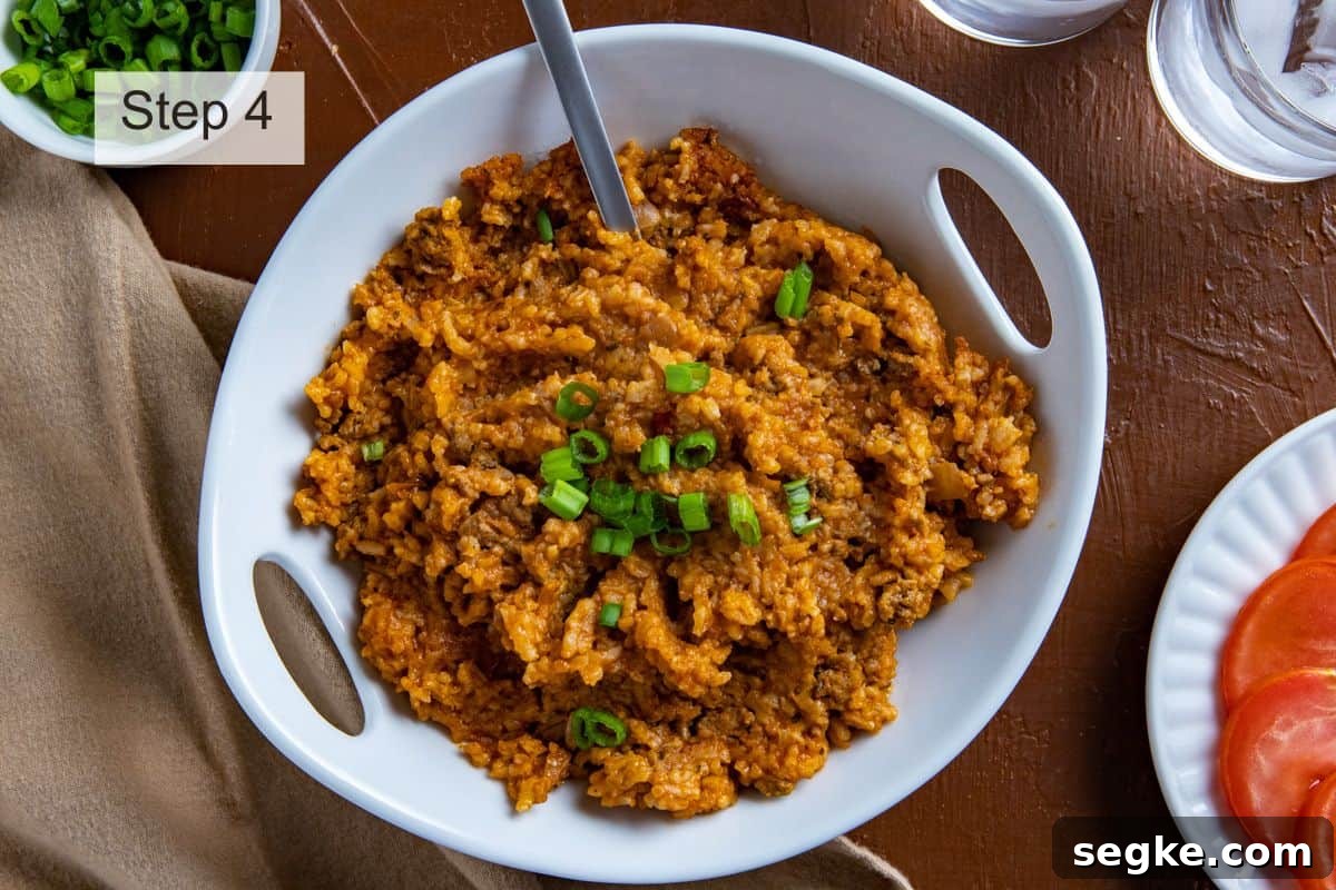 Cooked Spanish Rice in a white serving bowl with spoon inserted into the mixture. Sliced green onions on the side. Sliced tomatoes on the side.